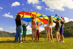 Quelle: unsplash.com/@artem_kniaz, https://unsplash.com/de/fotos/gruppe-von-frauen-die-tagsuber-auf-grunem-rasen-stehen-DqgMHzeio7g eine Gruppe Kinder steht im Kreis mit einem bunten Tuch